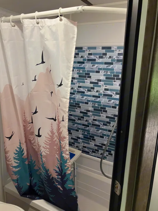 RV rental shower: a cozy bathroom with a nature-themed curtain, mosaic tile, and shower chair.. Riverside RV Retro 2021