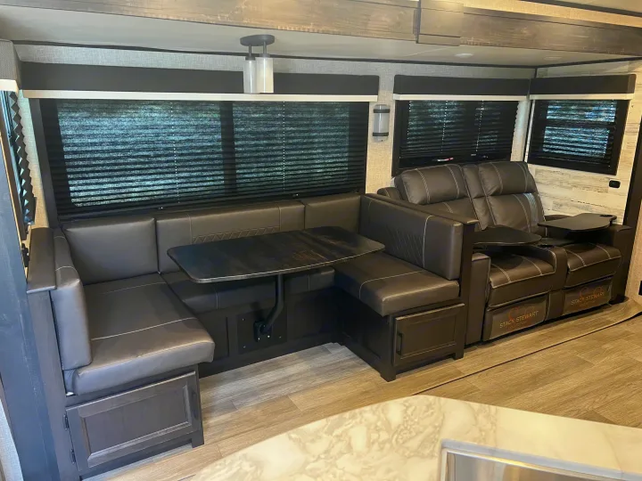 Inside this RV rental: a dark leather U-shaped dinette with a table, plus comfy reclining theater seats with trays.. Jayco White Hawk 2022