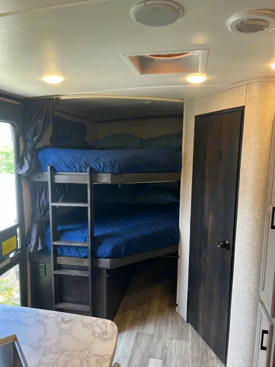 RV rental: Interior shot showing cozy bunk beds with blue bedding, a ladder for access, and a dark wood door.. Jayco White Hawk 2022