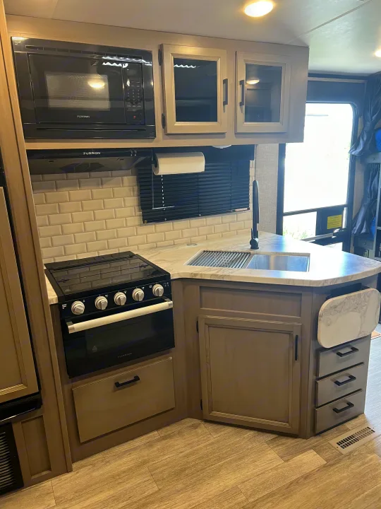 A modern RV rental kitchen with black Furrion appliances, light cabinetry, marble-look countertops, and subway tile backsplash.. Jayco White Hawk 2022