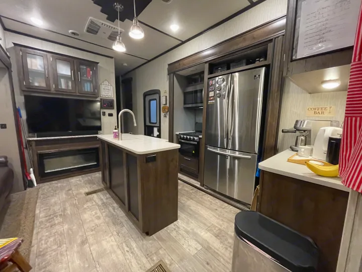 Inside an RV rental: kitchen island, stainless fridge, TV, fireplace, & coffee bar.. Crossroads RV Volante 2020