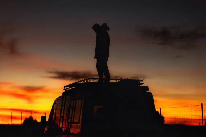 A person stands silhouetted on an RV rooftop against a vibrant orange and red sunset. Perfect for your next rv rental adventure.. Sportsmobile Regular Body 4X4 2017
