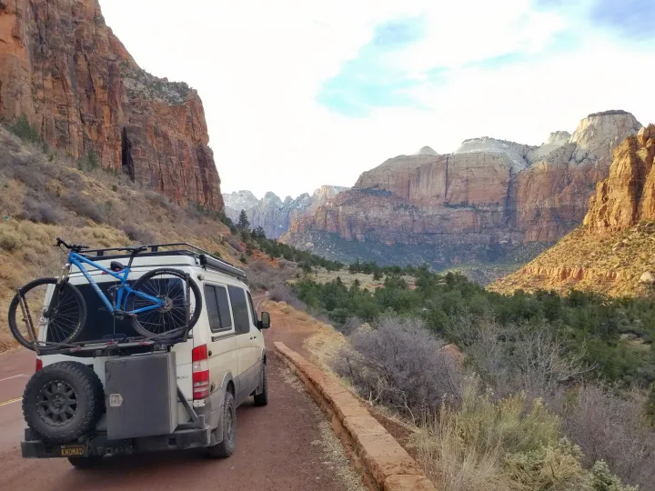 White camper van with bike on back, an ideal RV rental, on a dirt road in a stunning mountainous desert landscape.. Sportsmobile Regular Body 4X4 2017