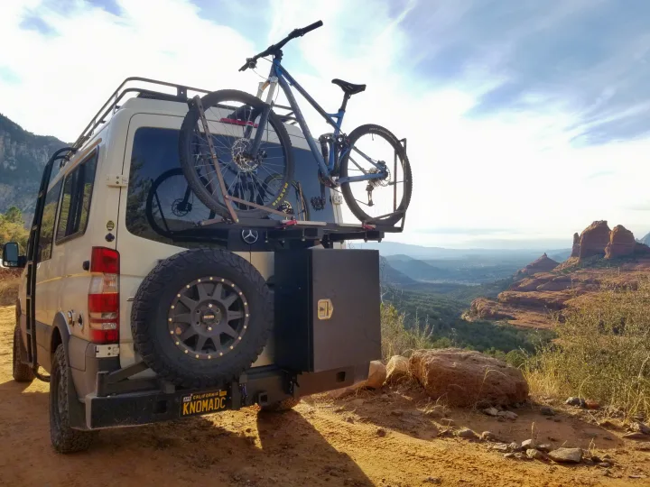 White Mercedes Sprinter rv rental van with a mountain bike & spare tire, parked at a breathtaking red rock overlook.. Sportsmobile Regular Body 4X4 2017