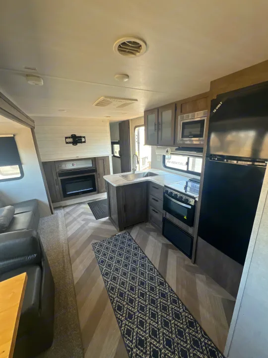 Modern RV rental interior: Full kitchen, cozy living room, electric fireplace, and stylish flooring.. Forest River Wildwood 2020