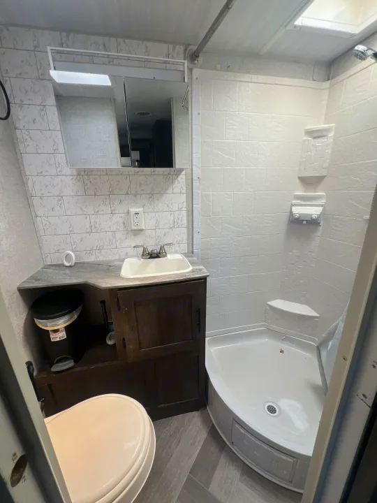 Compact and clean RV rental bathroom with a corner shower, toilet, sink, and vanity. Bright and functional.. Forest River Wildwood 2020