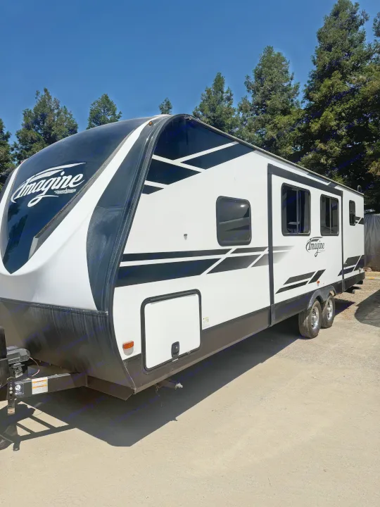 Explore the outdoors with this Imagine travel trailer RV rental, showcasing its modern black and white design parked on gravel.. Grand Design Imagine 2021