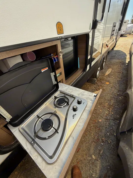Outdoor kitchen in an RV rental, featuring a pull-out stove, mini-fridge, and storage for camping essentials.. Grand Design Imagine 2021