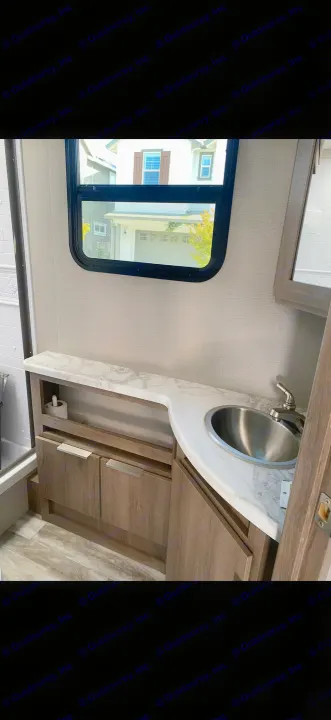 RV rental bathroom with a white marble-look vanity, stainless steel sink, wooden cabinets, and window.. Grand Design Imagine 2021