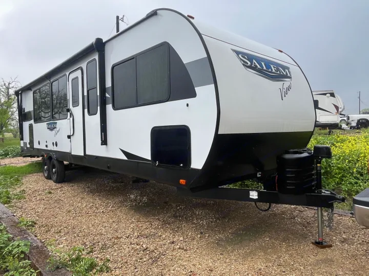 White travel trailer RV rental, parked on gravel. This Salem View RV features an awning and windows, ready for adventures.. Forest River Salem View 2024