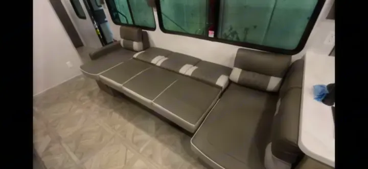 Long grey sofa and dinette area visible in a modern RV rental interior. Ideal for comfortable journeys.. Forest River Salem View 2024