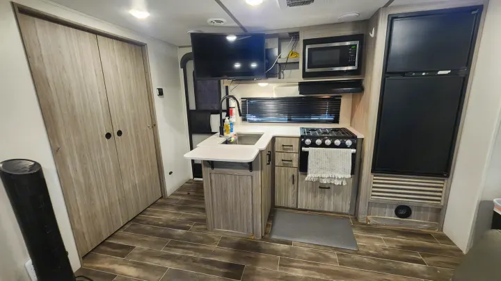 Inside this RV rental: a modern kitchen with a sink, stove, microwave, fridge, and a TV, opposite a large wardrobe.. Keystone RV Passport SL 2022