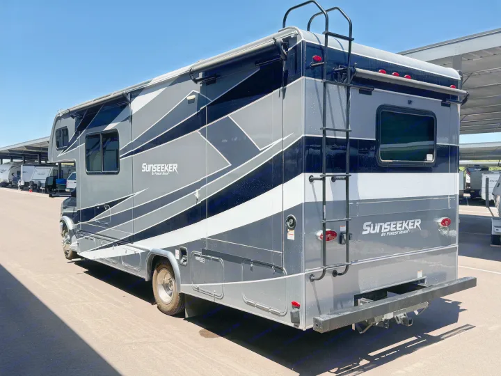 Sleek gray and black Sunseeker RV rental, equipped with a rear ladder and side awning, parked outdoors under clear sky.. Forest River Sunseeker Classic 2021
