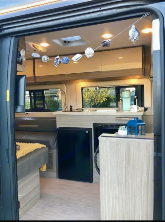 View inside a clean RV rental: compact kitchen, seating/bed, and bright interior lights. Perfect for road trips.. Jayco Swift 2021