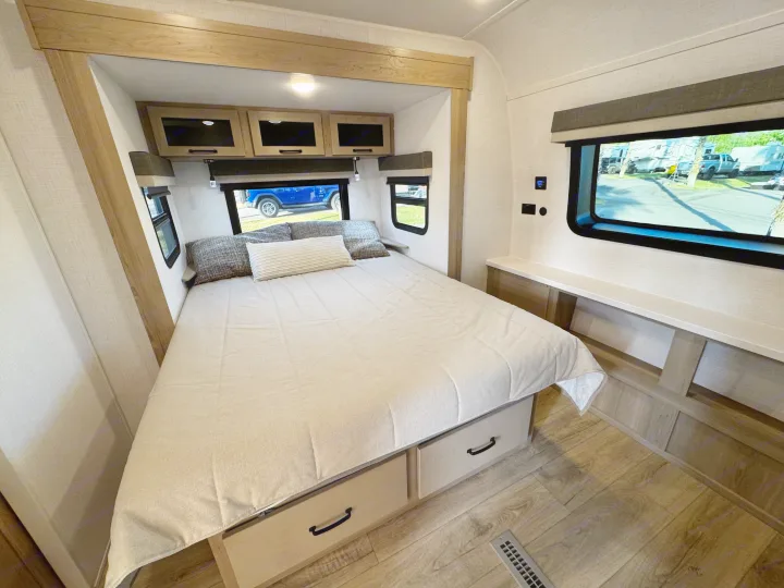 Cozy RV rental bedroom featuring a large bed with under-bed storage, overhead cabinets, and windows with scenic views.. Forest River Rockwood Ultra Lite 2024