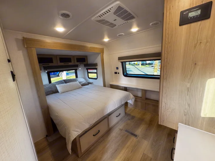 Modern RV rental bedroom with a queen bed, under-bed storage, and bright windows, plus a solar panel controller on the wall.. Forest River Rockwood Ultra Lite 2024