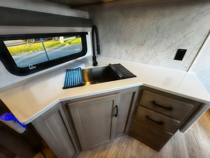 Modern RV rental kitchen with white counters, stainless sink, and light wood cabinets, perfect for travel.. Forest River Rockwood Ultra Lite 2024