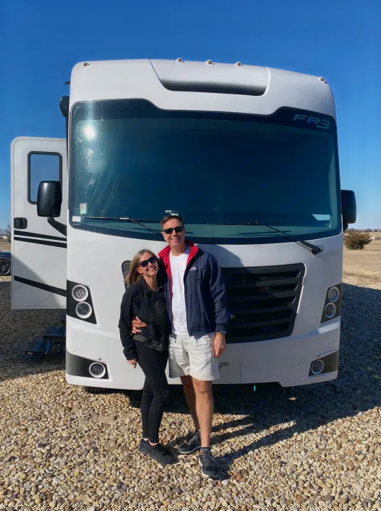 Smiling couple poses with their spacious white RV, ideal for a memorable **RV rental** adventure on a clear day.. FR3 FR3 Motorhome 2022