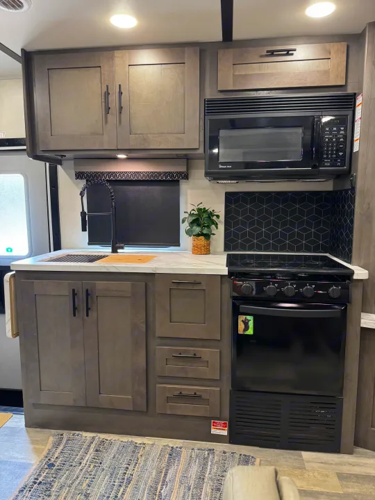Modern RV rental kitchen showcasing grey cabinets, microwave, oven, and sink with geometric backsplash.. FR3 FR3 Motorhome 2022
