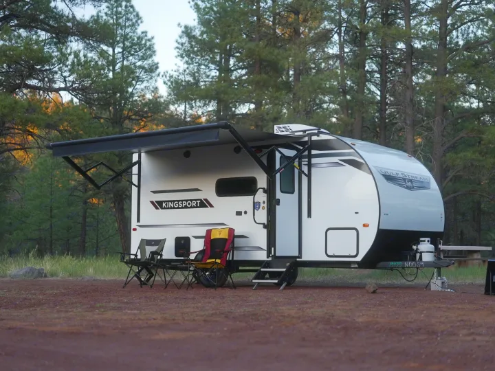 This rv rental, a white Gulf Stream Kingsport travel trailer, is set up with an awning and chairs in a peaceful pine forest.. Gulf Stream Kingsport Lite 199DD 2025