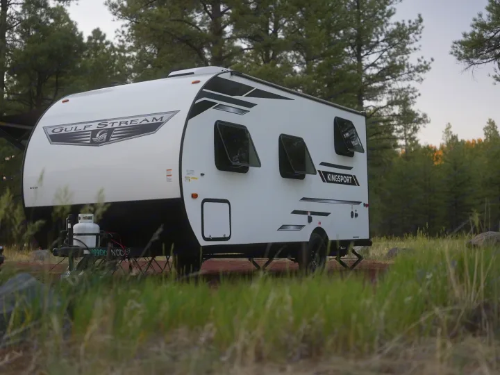 A white Gulf Stream Kingsport RV rental is parked in a serene forest campsite. Ready for adventure and nature.. Gulf Stream Kingsport Lite 199DD 2025