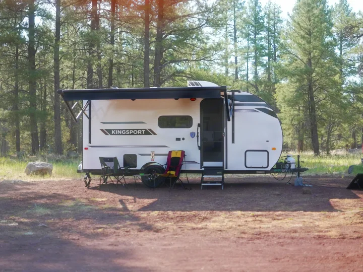 A white Kingsport rv rental trailer with an awning, chairs, and table at a serene pine forest campsite.. Gulf Stream Kingsport Lite 199DD 2025