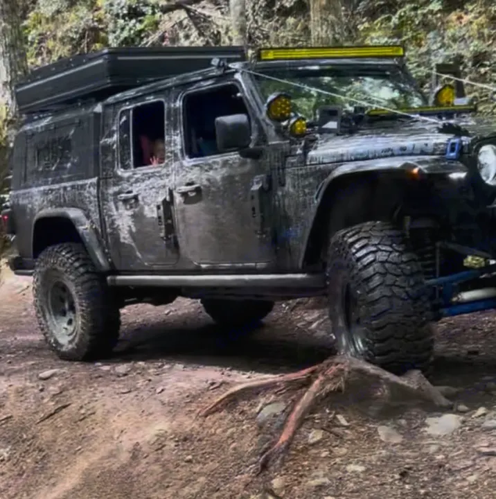 Muddy Jeep Gladiator with rooftop tent on a forest trail, perfect for an adventurous rv rental or overlanding trip.. Dodge Jeep Unlimited X 4x4 2021
