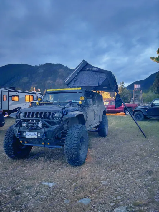 An off-road Jeep with a rooftop tent at a mountain campsite, near an RV rental, under a moody, cloudy sky.. Dodge Jeep Unlimited X 4x4 2021
