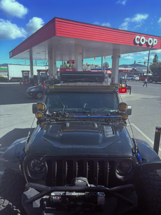 A rugged black Jeep with an RV-style rooftop tent at a CO-OP gas station, ready for an adventurous rv rental journey.. Dodge Jeep Unlimited X 4x4 2021