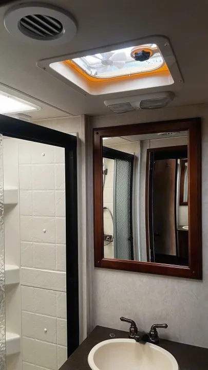 RV rental's compact bathroom with shower stall, sink, framed mirror, and overhead ventilation system visible.. Forest River Coachmen Mirada 2013