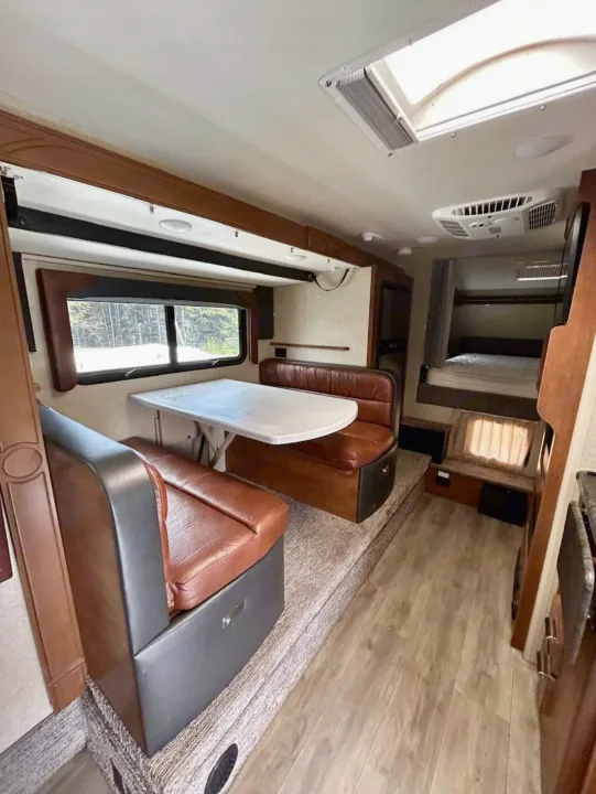This RV rental features a bright interior with a dining booth, table, and a cozy bed. Experience comfortable travel.. Lance 1172 2017