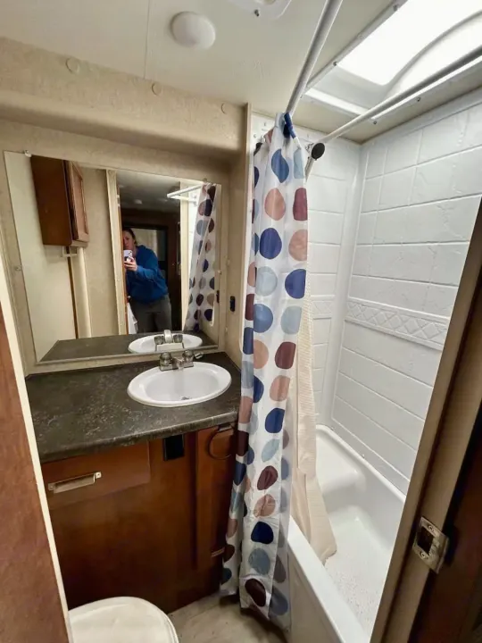 A compact and clean RV rental bathroom with a sink, large mirror, and shower/tub combo with a polka-dot curtain.. Lance 1172 2017
