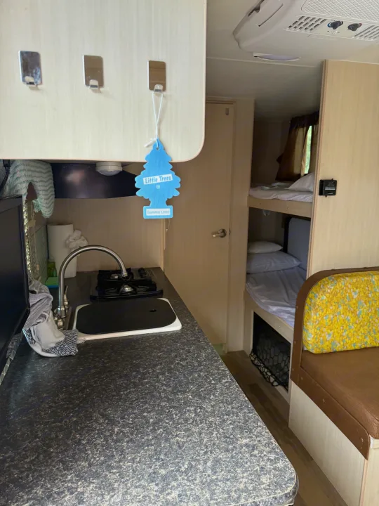 Inside an RV rental: a compact kitchen with sink, stovetop, air freshener, plus cozy bunk beds & dinette for travel.. Minnie Micro Minnie 2017