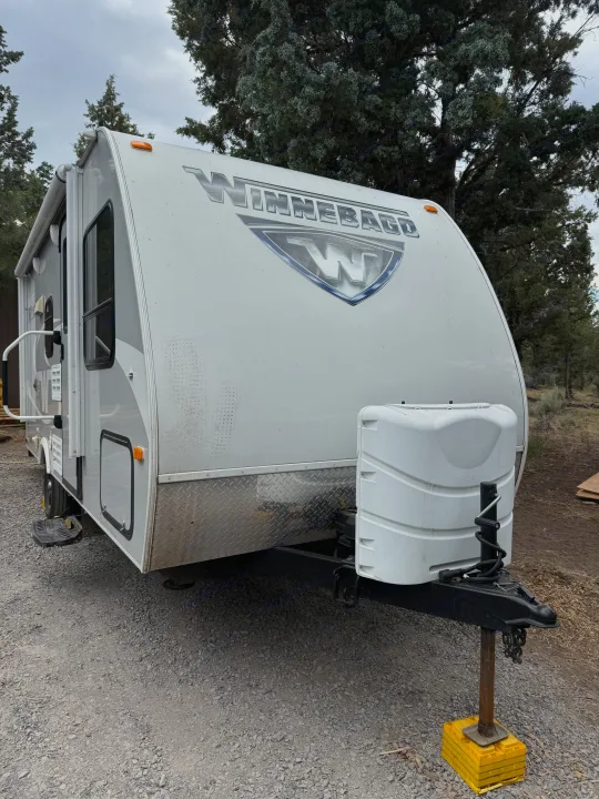 This Winnebago travel trailer, perfect for your next rv rental, is parked on gravel amidst trees.. Minnie Micro Minnie 2017