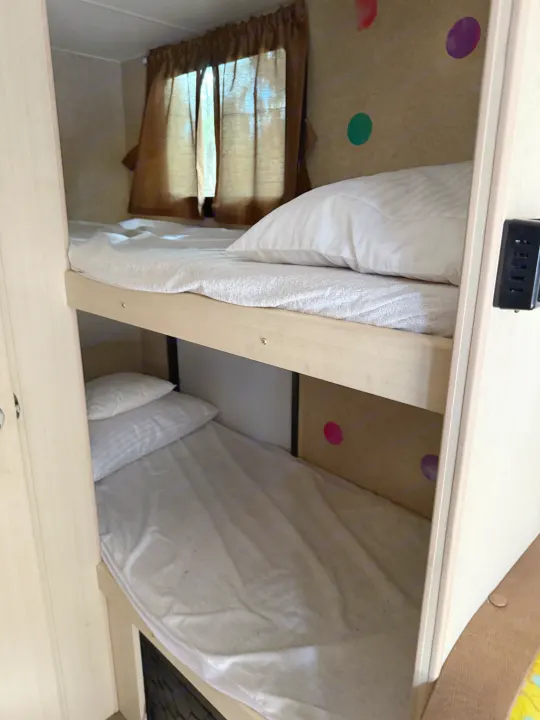 Cozy bunk beds in an RV rental, featuring white bedding, a window with brown curtains, colorful polka dots, and a power strip.. Minnie Micro Minnie 2017