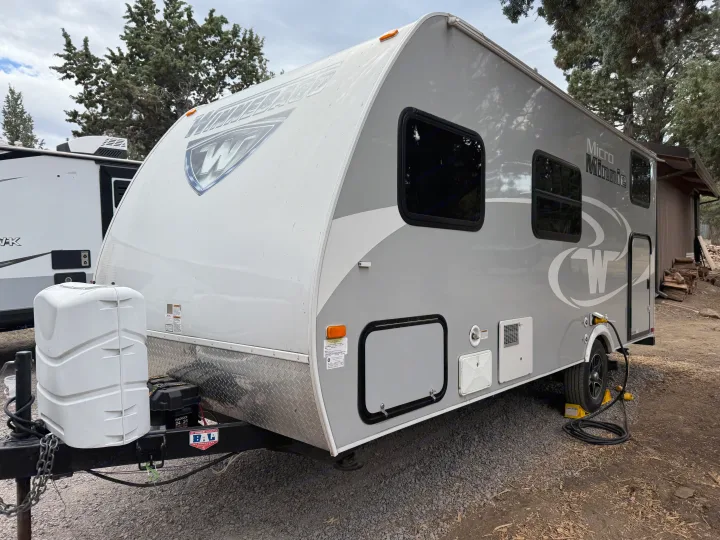 Winnebago Micro Minnie travel trailer, a great rv rental choice. This gray and white camper is parked on gravel at a campsite.. Minnie Micro Minnie 2017