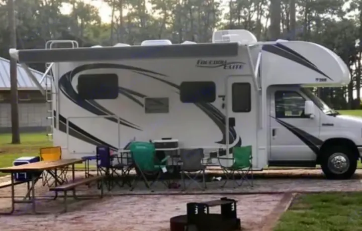 Freedom Elite RV rental parked at a peaceful campsite with an outdoor picnic setup, tables, and chairs.. Coachmen Freedom Elite 2019