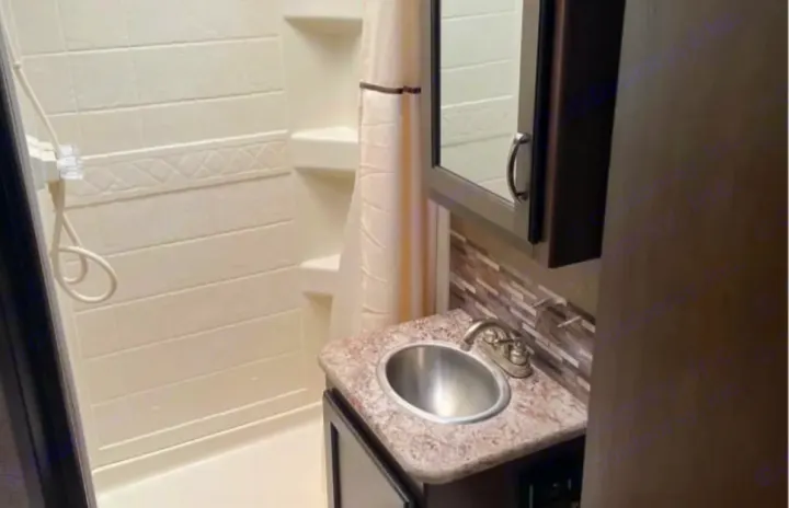 Explore a compact RV rental bathroom featuring a clean shower stall, a small vanity with a sink, and a mirrored cabinet.. Coachmen Freedom Elite 2019