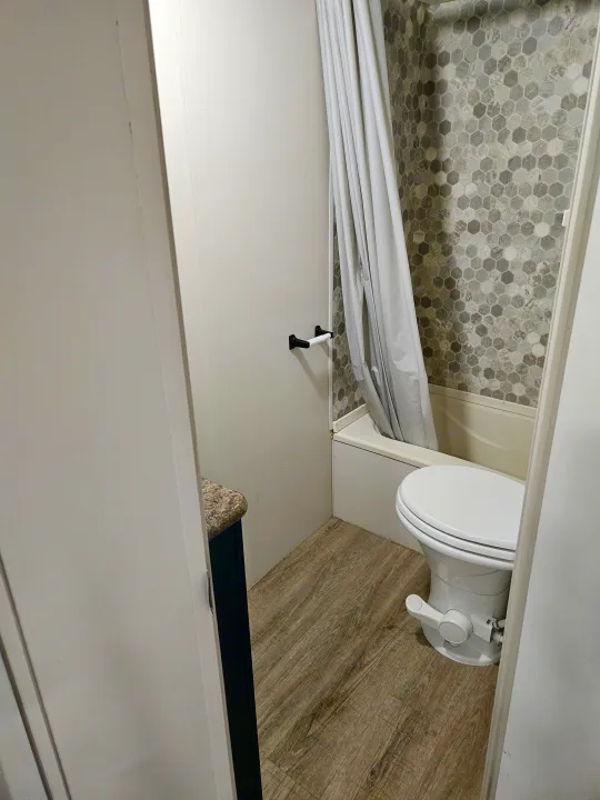 Compact RV rental bathroom featuring a hexagonal tile shower, modern toilet, and wood-look flooring.. Spree Escape 2014