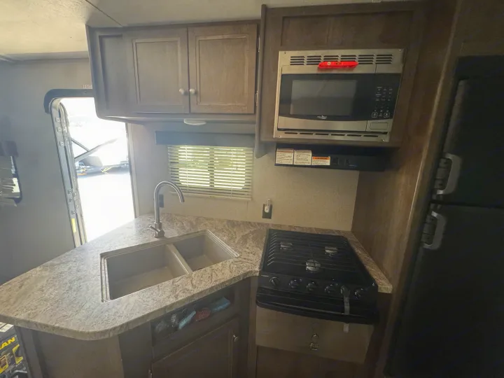 Modern RV rental kitchen: stainless steel microwave, gas stove, dual sink, and wood cabinets.. Dutchmen Coleman Lantern 2018