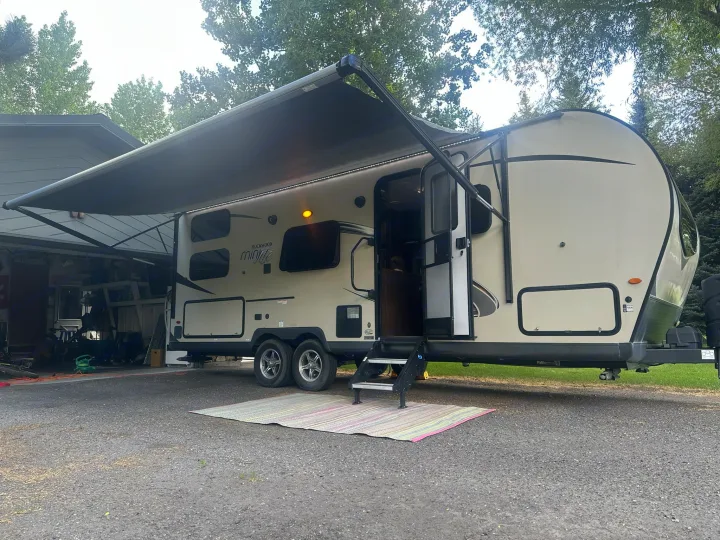 Light-colored RV rental with extended awning & steps, parked on asphalt. Ideal for camping & travel getaways.. Forest River Rockwood Mini Lite 2020