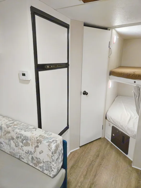 RV rental interior featuring a sofa, refrigerator, thermostat, and bunk beds with lights. A practical and cozy space.. Spree Escape 2014