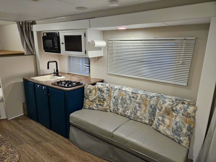 This RV rental's inviting interior features a compact kitchen with a sink, stove, and microwave, alongside a comfy sofa.. Spree Escape 2014