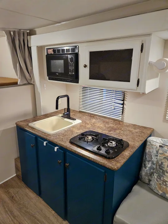 Compact RV kitchen with sink, stove, microwave, and teal cabinets, ideal for an rv rental getaway.. Spree Escape 2014