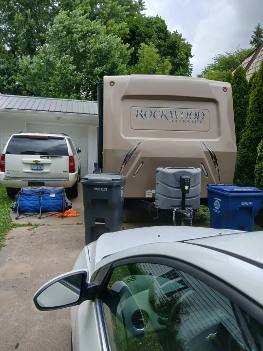 Spacious beige Rockwood travel trailer, an excellent RV rental option, parked with a white Suburban and bins in a residential driveway.. Forest River Rockwood Ultra Lite 2016