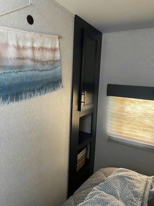Cozy RV rental bedroom: showing a clever storage cabinet, wall hanging, and comfortable bed.. Forest River Cherokee 2022