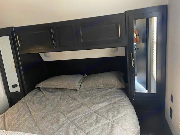 Cozy RV rental bedroom features a comfortable bed, overhead black cabinets, and mirrored wardrobes for compact travel comfort.. Forest River Cherokee 2022