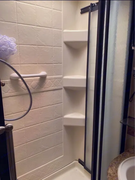 Compact shower in an RV rental, featuring tiled walls, a grab bar, corner shelves, and frosted door.. Hurricane F53 2010