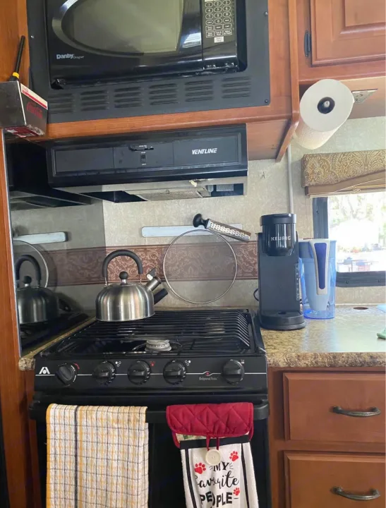 An RV rental kitchen features a compact microwave, stove, Keurig, and water pitcher. Space-saving appliances for comfortable travel cooking.. Hurricane F53 2010
