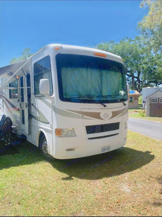 This spacious white RV rental, with an awning extended, is parked on green grass under a clear blue sky. Ideal for road trips.. Hurricane F53 2010